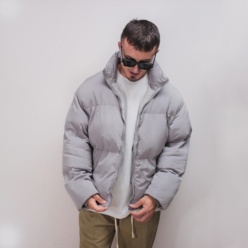 Man wearing a gray puff jacket with white shirt and khaki pants.