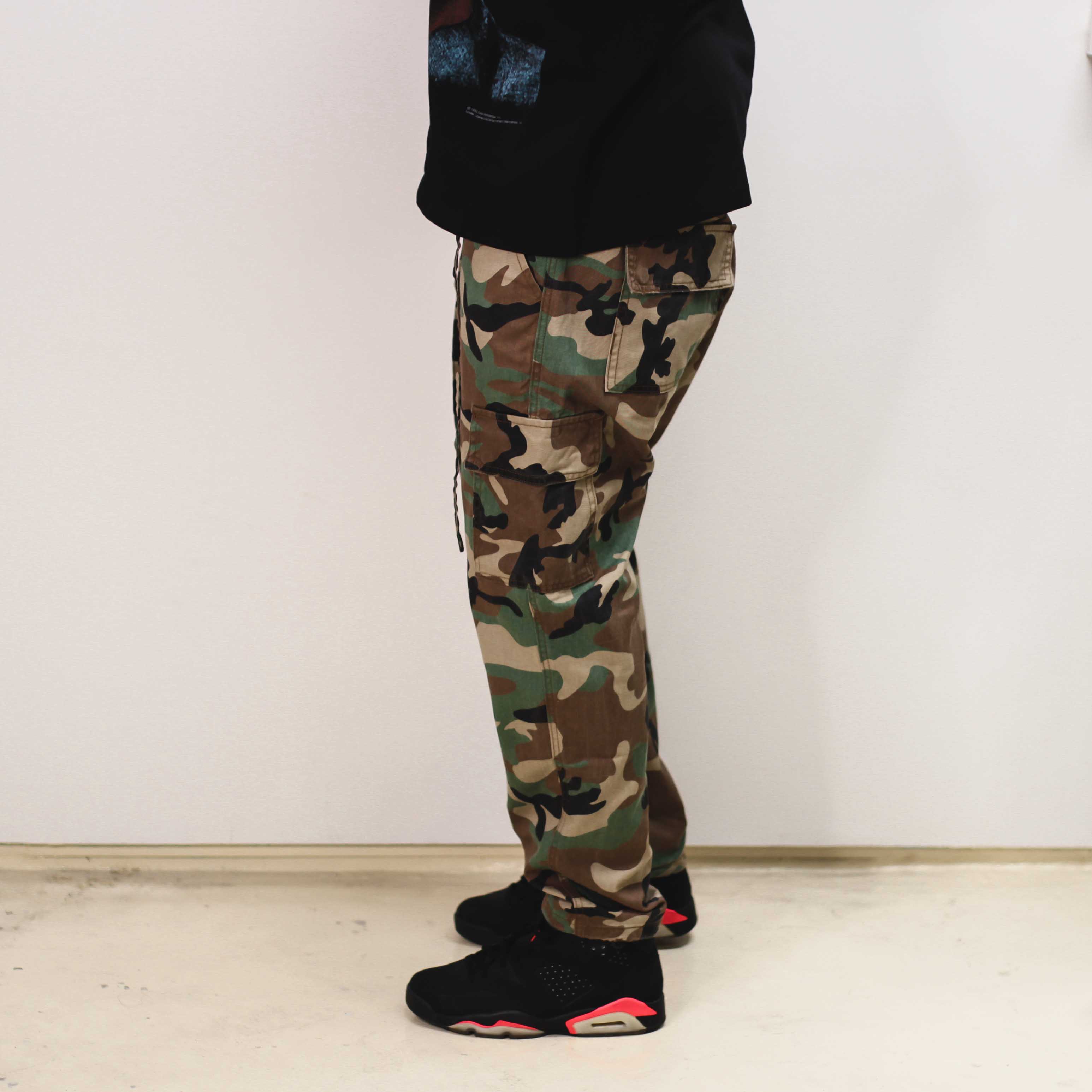 Side view of camo trousers paired with black sneakers.