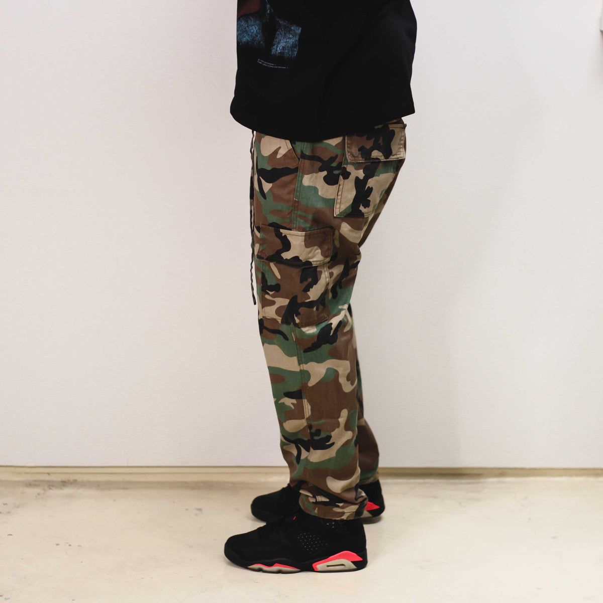 Side view of camo trousers paired with black sneakers.