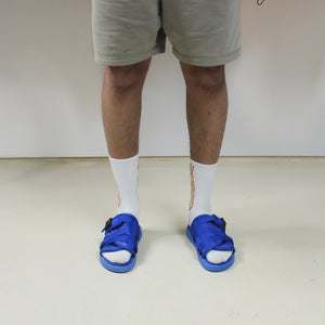 tanned leg model facing forward, white socks, gray shorts, cobalt blue adjustable tightening strap sliders