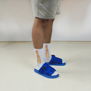 tanned leg model wearing cobalt blue strap sliders with white flame socks on, gray shorts