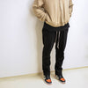 model wearing cotton black drawstring pant with tan zip-up hoodie, hands in pockets, jordan satin trainer on foot