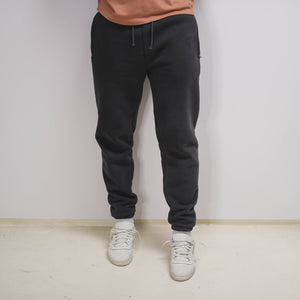 model wearing unisex tailored jogger pants in core gray colour, adidas calabasas cream shoes on foot, copper coloured t-shirt