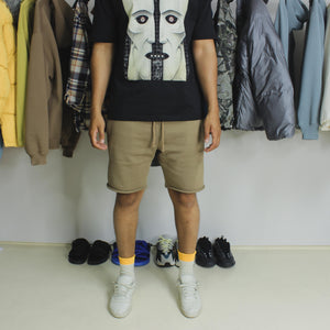 model wearing camel coloured shorts with yeezy creamy calabasas power phase trainers, black pink floyd t-shirt, multi-coloured clothing hung up in background