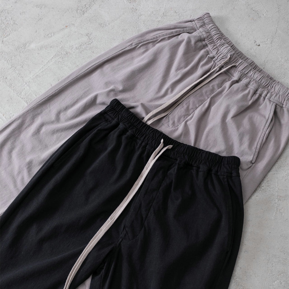 Black drawstring pant on display with a taupe pair on a textured surface.