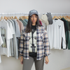 female model with range of hanging clothes in background, wearing multi-coloured flannel, gray limn clothing hat,, black t-shirt with pink floyd graphic, ash joggers