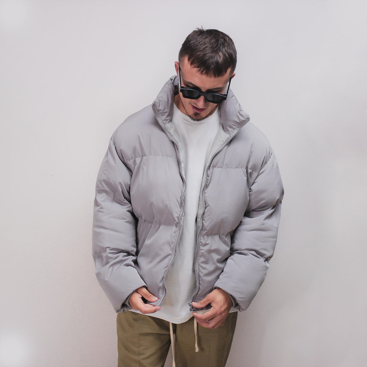 Man wearing a gray puff jacket with white shirt and khaki pants.